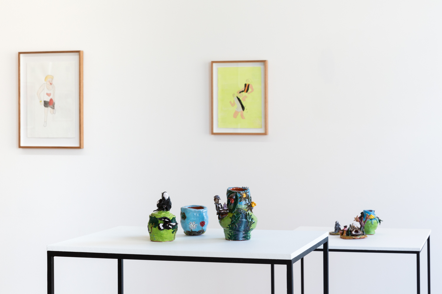A photo of 3 ceramics atop a white plinth. In the background is a framed artwork on a gallery wall