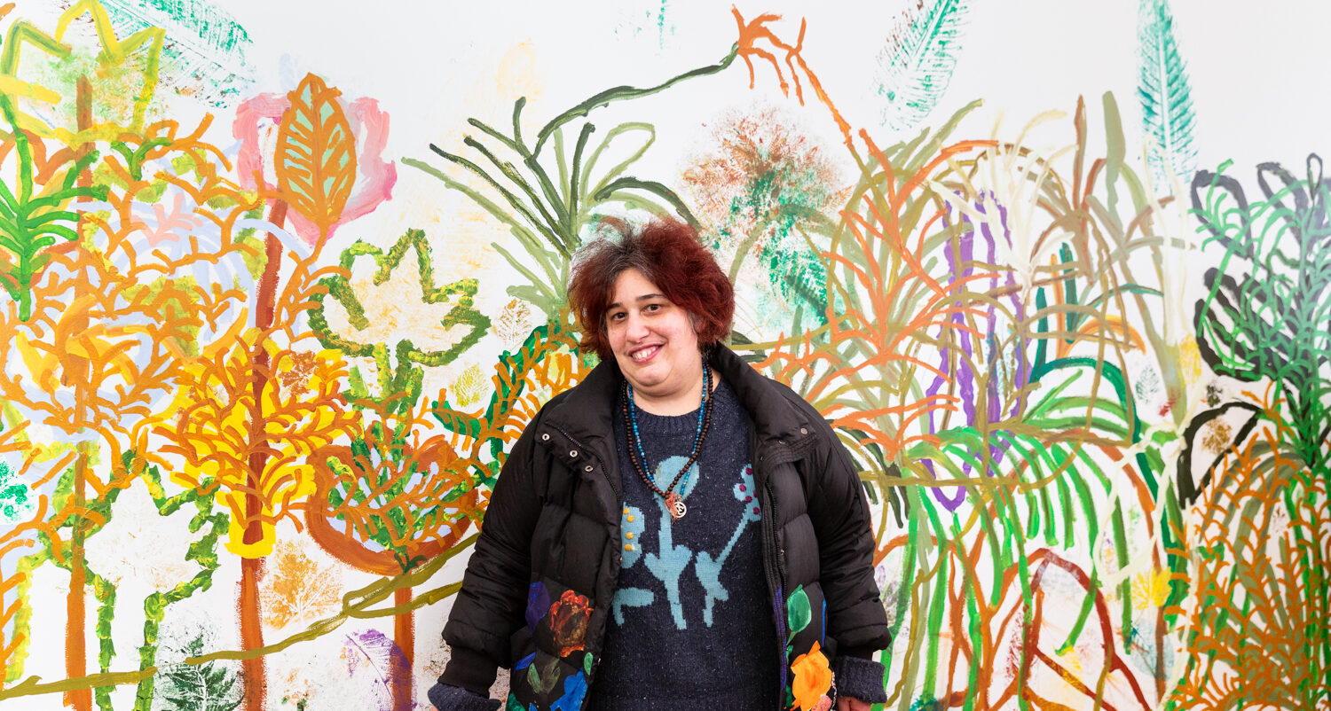 Georgia Szmerling in front of her painted mural for the Plant Life exhibition at Arts Project Australia's gallery in collingwood yards